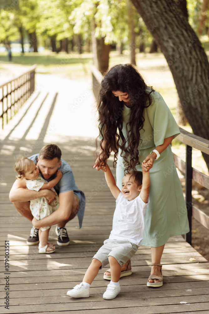 Happy family with little kids at the park, caring father hugging cute baby girl, lovely mother hold hands of overjoyed son, enjoy happy weekend outdoors, parenting concept Happy family with little kids at the park, caring father hugging cute baby girl, lovely mother hold hands of overjoyed son, enjoy happy weekend outdoors, parenting concept