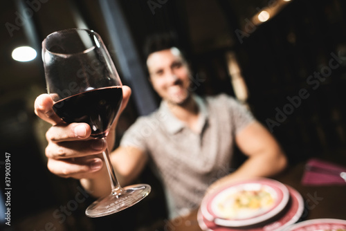 Handsome man doing toast with red wine in restaurant  looking at camera