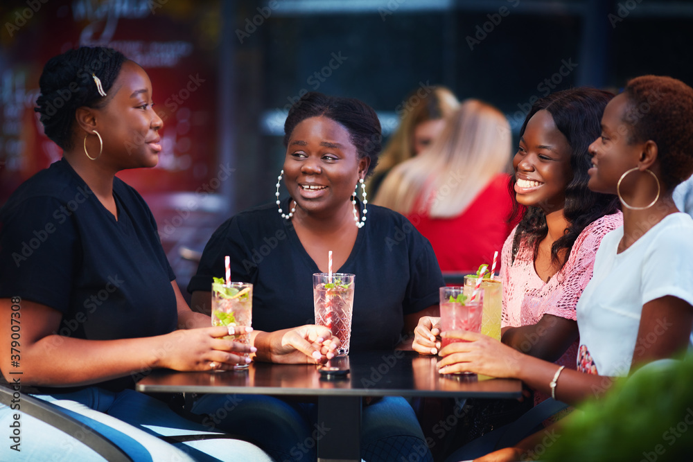 Happy Friends, African American Women sitting together at the outdoor restaurant at summer day
