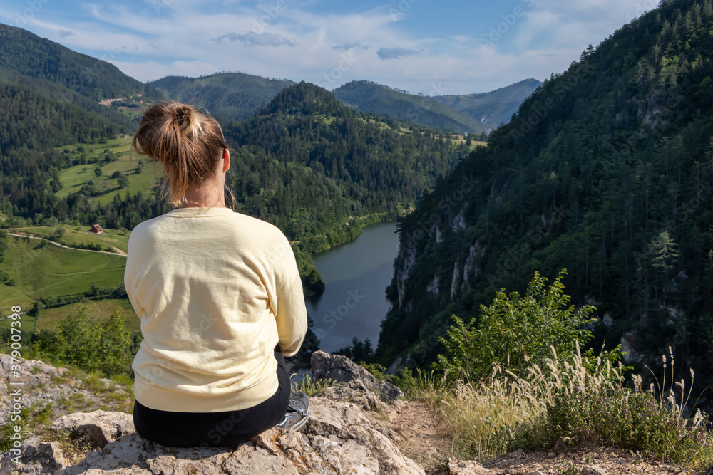 Naklejka premium Young girl in the nature. Back view portrait of a single woman watching the Spajici lake from the height in west Serbia