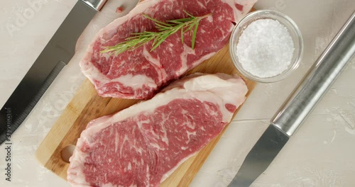 On a striploin steak a man's hand puts rosemary. 