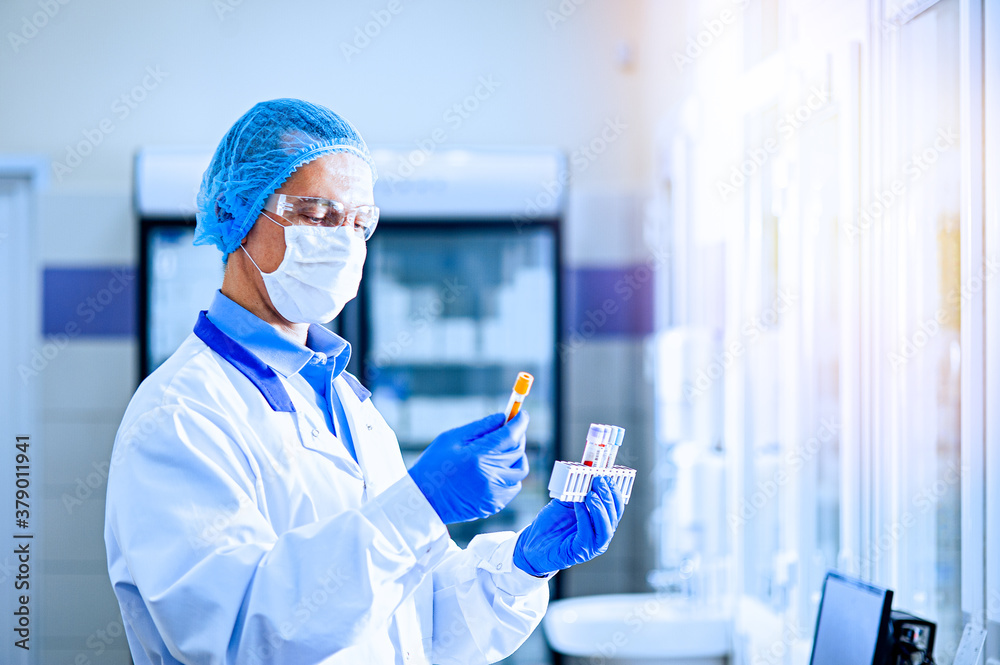 A medical worker, a laboratory assistant in a protective mask, visor, disposable cap and rubber gloves stands in a laboratory, hospital. A medical worker, a laboratory assistant in a protective mask, visor, disposable cap and rubber gloves stands in a laboratory, hospital.