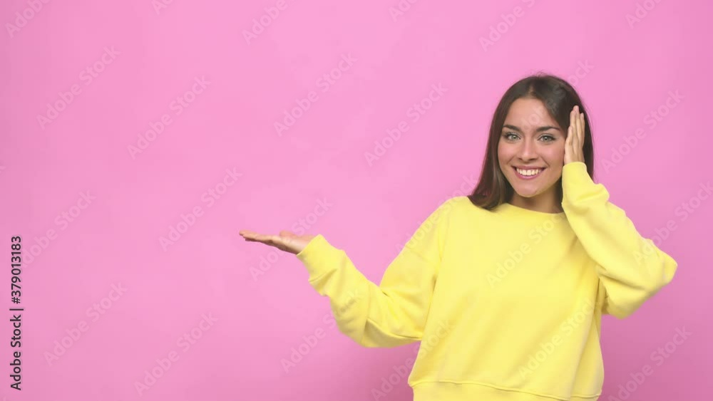 Young cute woman holds copy space on a palm, keep hand over cheek amazed and delighted