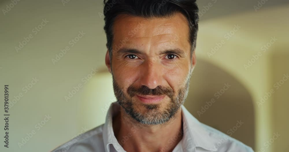 Close up of handsome self confident happy man is smiling in camera in a living room at home.