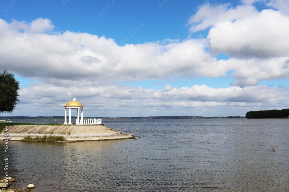 Summer day on the shore of a beautiful lake. Blue sky with sun over water. Recreation and ecology concept.
