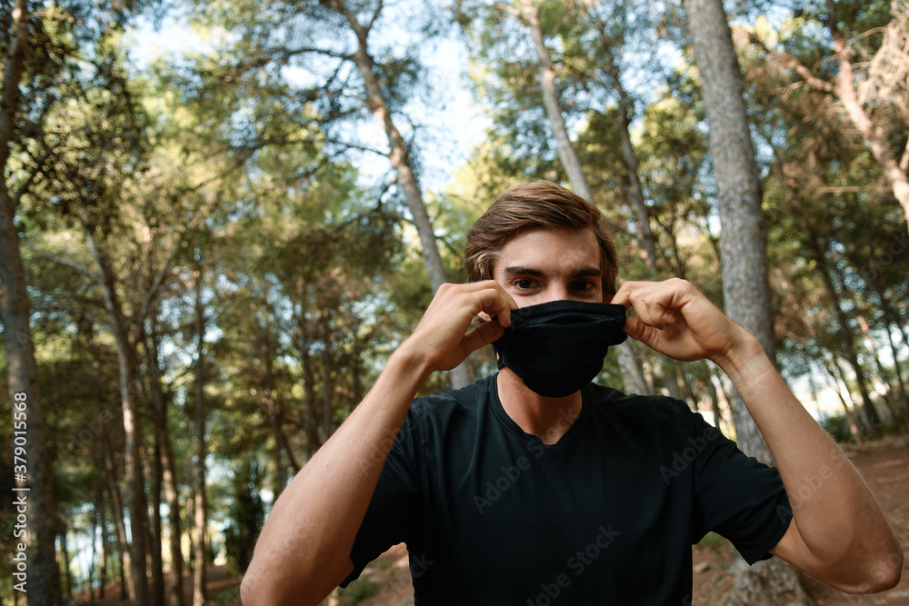 Joven atleta ajustándosela la mascarilla en el bosque Joven atleta ajustándosela la mascarilla en el bosque