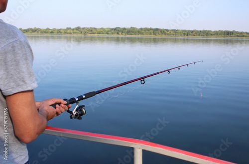 close-up of male hands of a young man holding a fishing rod leaning on a railing on the river bank in the morning. The theme of fishing, recreation, leisure, outdoor activities
