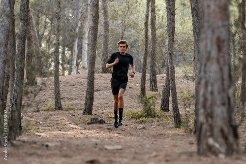 Atleta joven corriendo por un bosque, vestido con una camiseta negra y pantalón corto negro