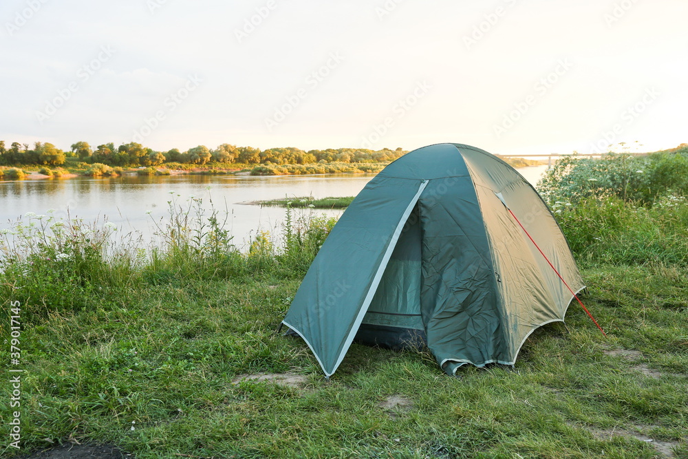 green tourist tent is on the bank of the river at sunset