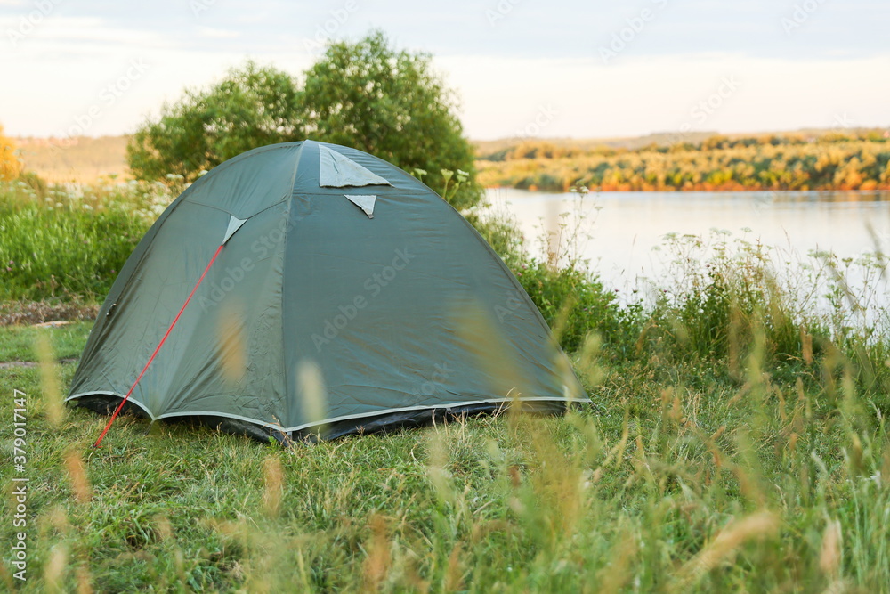 green tourist tent is on the bank of the river at sunset