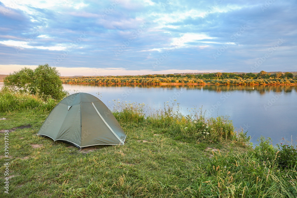 green tourist tent is on the bank of the river at sunset