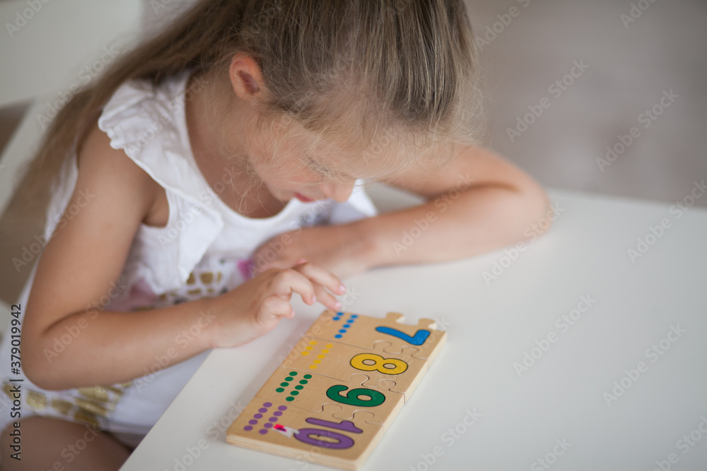 Little cute preschooler child girl playing educational games with wooden mathematical multicolored figures preparing for school in kindergarten while sitting at table. Back to school concept. Little cute preschooler child girl playing educational games with wooden mathematical multicolored figures preparing for school in kindergarten while sitting at table. Back to school concept.