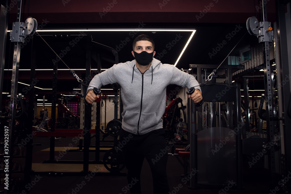 Muscular man workout in gym doing exercises for chest, cable crossover. Strong male in medical mask