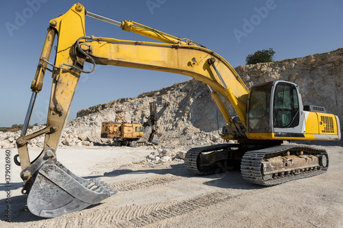 A large yellow tracked excavator is mining rock in a quarry.