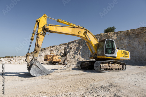 A large yellow tracked excavator is mining rock in a quarry.