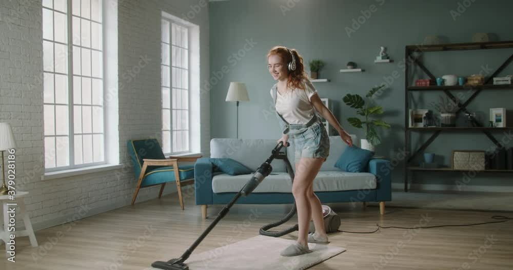 Young positive caucasian woman funnily dancing while cleaning the house. Cute girl enjoys tidying her home, using vacuum cleaner and listening to music - happy people 4k footage Young positive caucasian woman funnily dancing while cleaning the house. Cute girl enjoys tidying her home, using vacuum cleaner and listening to music - happy people 4k footage