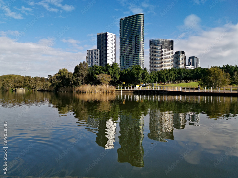 Beautiful view of a lake with reflections of luxury high-rise building, blue sky, clouds, and trees on water, lake Pavillion,  Sydney Olympic park, Sydney, New South Wales, Australia
