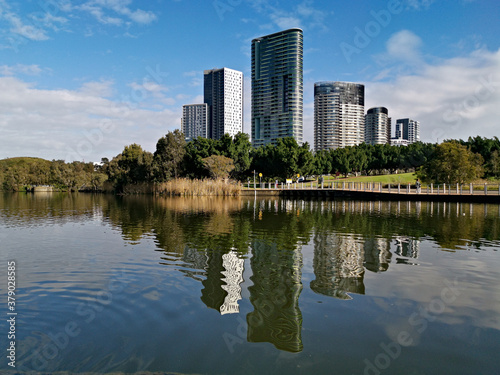 Beautiful view of a lake with reflections of luxury high-rise building, blue sky, clouds, and trees on water, lake Pavillion, Sydney Olympic park, Sydney, New South Wales, Australia 