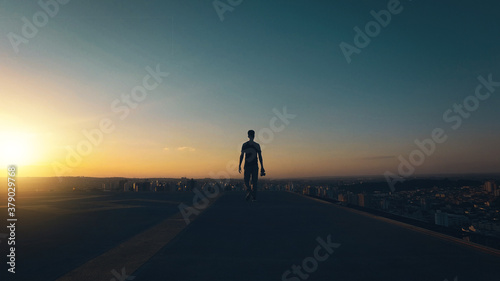 Silhouette of a man walking on top of the building at sunset and cloudy sky. Concept photographer man image.