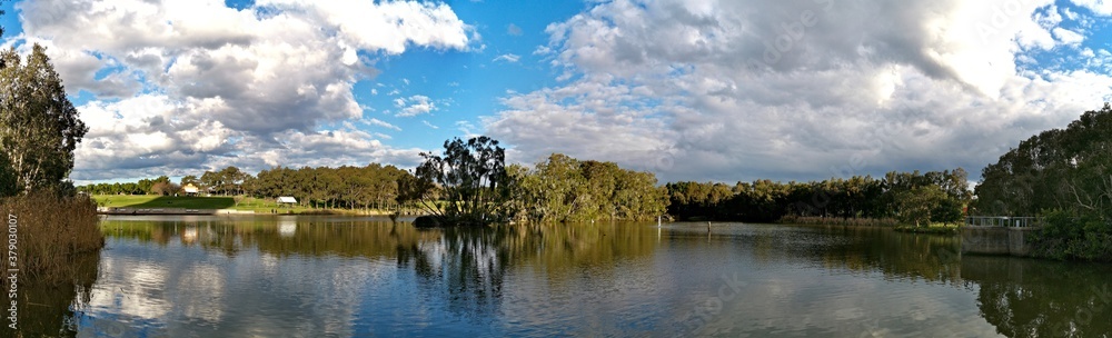 Beautiful panoramic view of a lake with reflections of blue sky, clouds, and trees on water, lake Pavillion, Sydney Olympic park, Sydney, New South Wales, Australia
