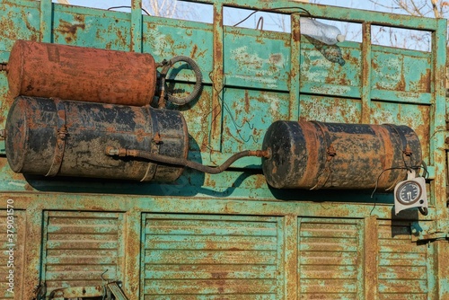 three old iron black and brown gas tanks in rust on the green metal side of the truck