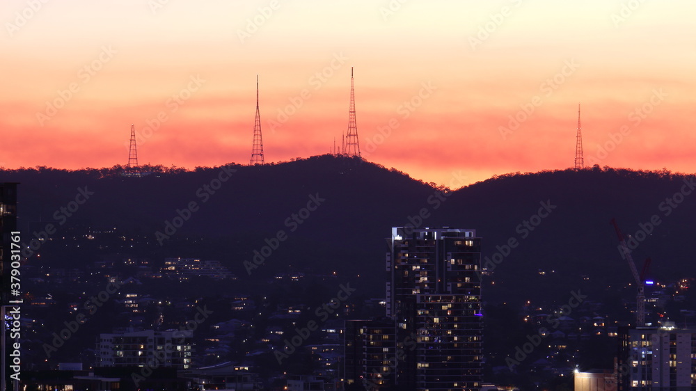 Fototapeta premium Silhouette of radio and tv transmission towers against the setting sun, on Mount Coot-Tha, with buildings in the foreground, in Brisbane, Queensland, Australia