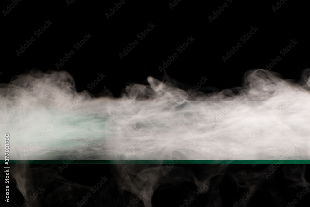 White smoke swirling spreads over the surface flowing down from the edges on a black background