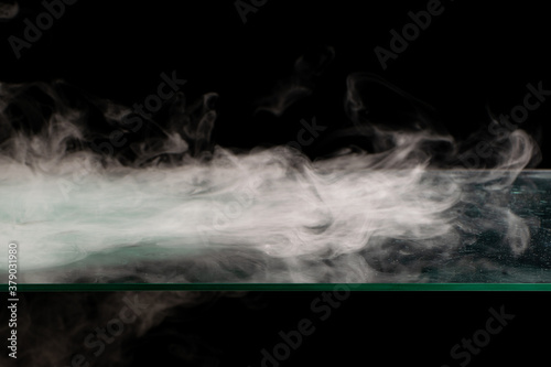White smoke swirling spreads over the surface flowing down from the edges on a black background