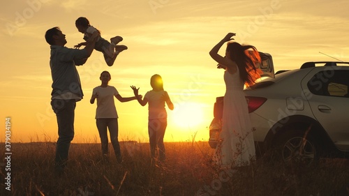 dad plays and throws joyful daughter into sky, mom and children dance at sunset. parents and children stopped for break by car. happy family travels by car. Car travel concept. healthy family