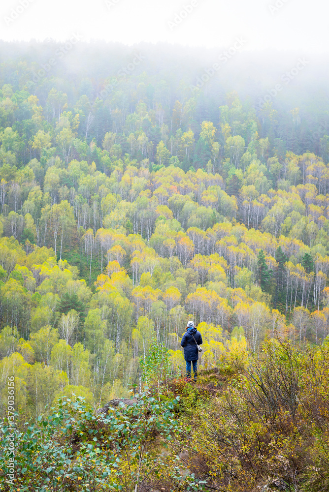 Fototapeta premium A woman on the mountain side looking at the forest of endless autumn taiga