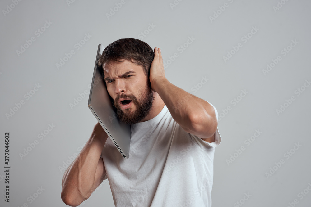 A man with a laptop in his hands on a light background in a white t-shirt emotions light background new technologies A man with a laptop in his hands on a light background in a white t-shirt emotions light background new technologies