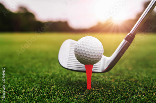 close up golf club and golf ball on green grass with sunrise background