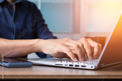 Man's hands typing on laptop keyboard with sun light effect.