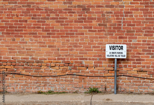 Antique grungy reddish brown brick wall texture background in a common bond brickwork pattern, with a visitor parking sign and copy space