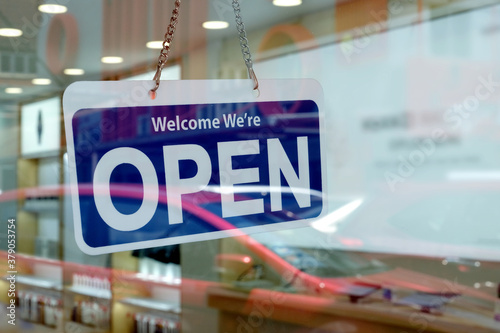 A 'Welcome We're Open' sign hanging on a glass entrance door of a shop selling electronic gadgets. Store with open for business signage welcoming customers to shop during its operating hours.