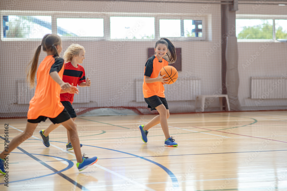 Kids in bright sportswear playing basketball together and running
