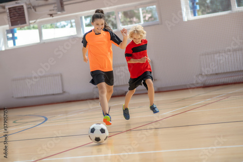 Three kids in sportswear running after the ball in the gym