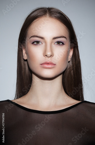Beauty people portrait. Female model of a natural skin, wear in black dress, looking at camera, over grey background.