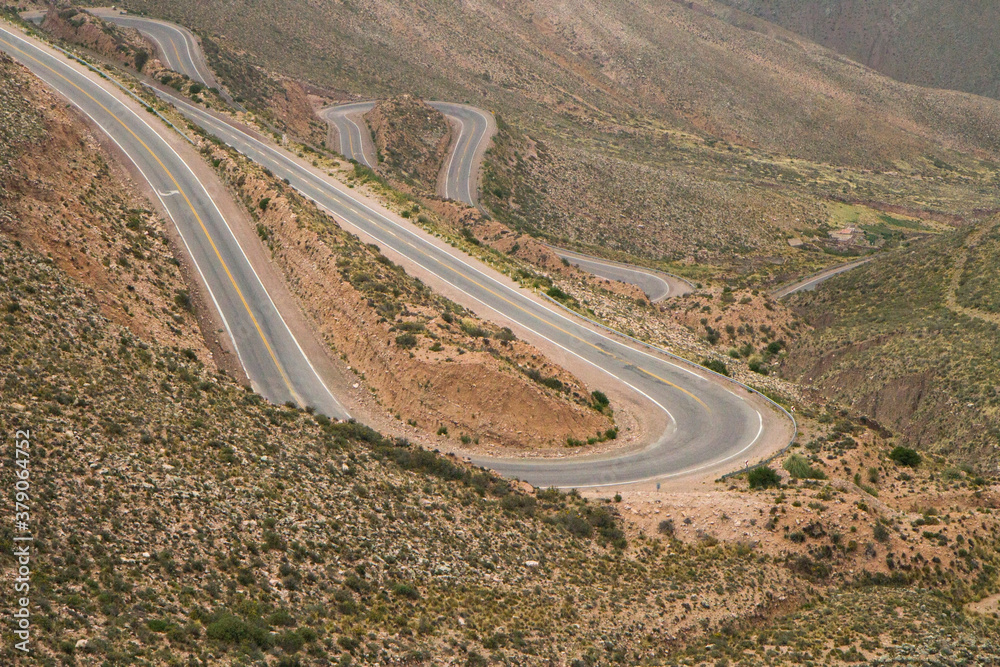 Empty desert road curves in the mountains. Driving along the asphalt route across the popular Lipan slope in Jujuy, Argentina. The curved highway across the arid desert, brown valley and mountains.