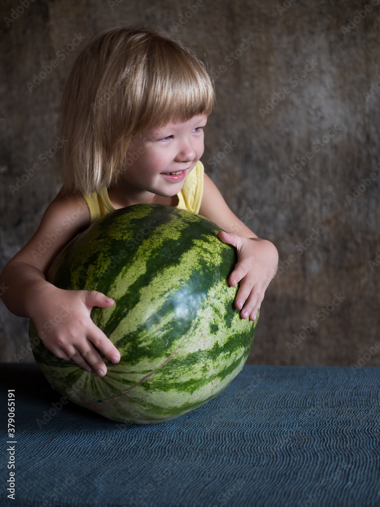 Fototapeta premium Funny blond boy hugs big watermelon lying on table with his hands