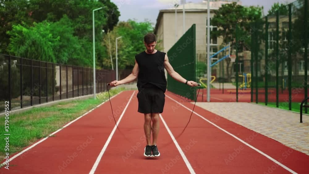 Fit, bearded man standing on running track outdoors on modern stadium doing exercise with skipping rope Fit, bearded man standing on running track outdoors on modern stadium doing exercise with skipping rope