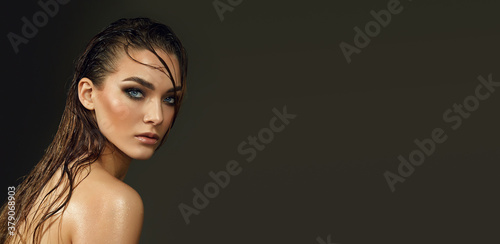 Beautiful young blue-eyed woman with wet skin and wet hair in the studio on a gray background. Close-up portrait.