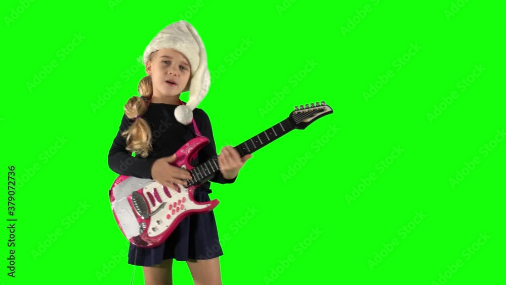 Little girl singing and playing toy guitar with Santa hat on Christmas concert Little girl singing and playing toy guitar with Santa hat on Christmas concert