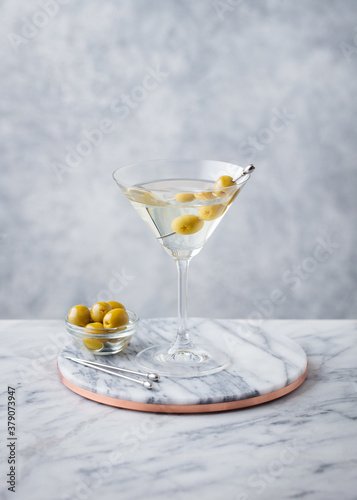 Martini cocktail with green olives on marble cutting board. Grey background. Copy space.