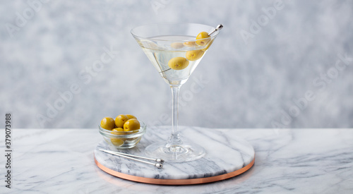 Obraz na plátně Martini cocktail with green olives on marble cutting board