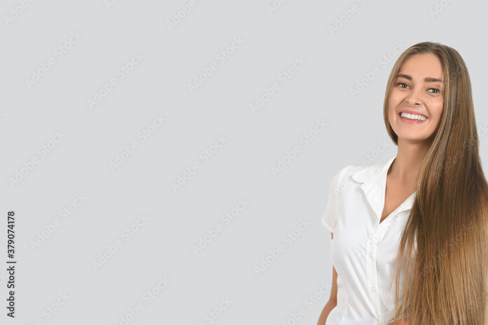 Beautiful young woman with long hair, dressed in a light blouse, smiling, looking at the camera. Portrait in the studio. The image has a blank space for your text. Beautiful young woman with long hair, dressed in a light blouse, smiling, looking at the camera. Portrait in the studio. The image has a blank space for your text.