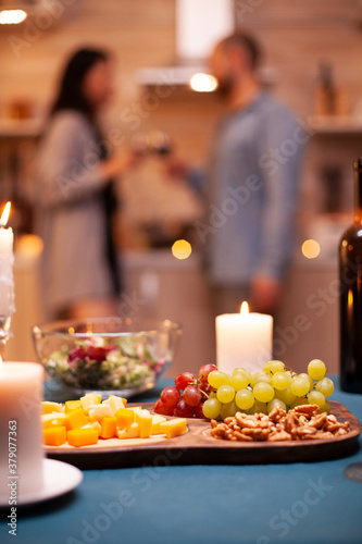 Close up of grapes and mix of cheese on wooden plate during couple romantic dinner.
