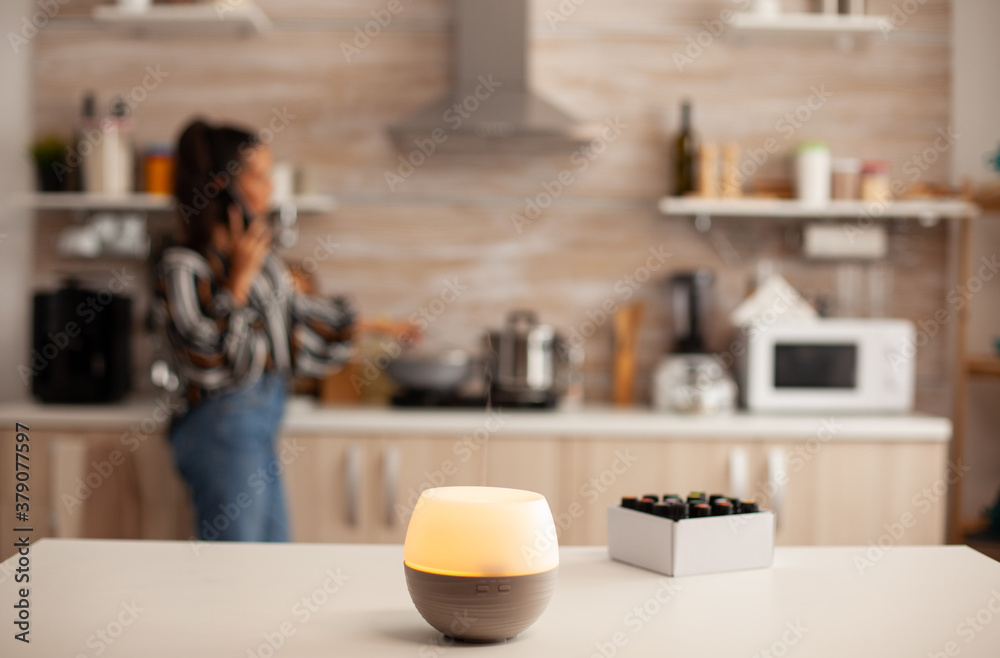 Diffuser spreading essential oils in kitchen and woman relaxing. Aroma health essence, welness aromatherapy home spa fragrance tranquil theraphy, therapeutic steam, mental health treatment Diffuser spreading essential oils in kitchen and woman relaxing. Aroma health essence, welness aromatherapy home spa fragrance tranquil theraphy, therapeutic steam, mental health treatment