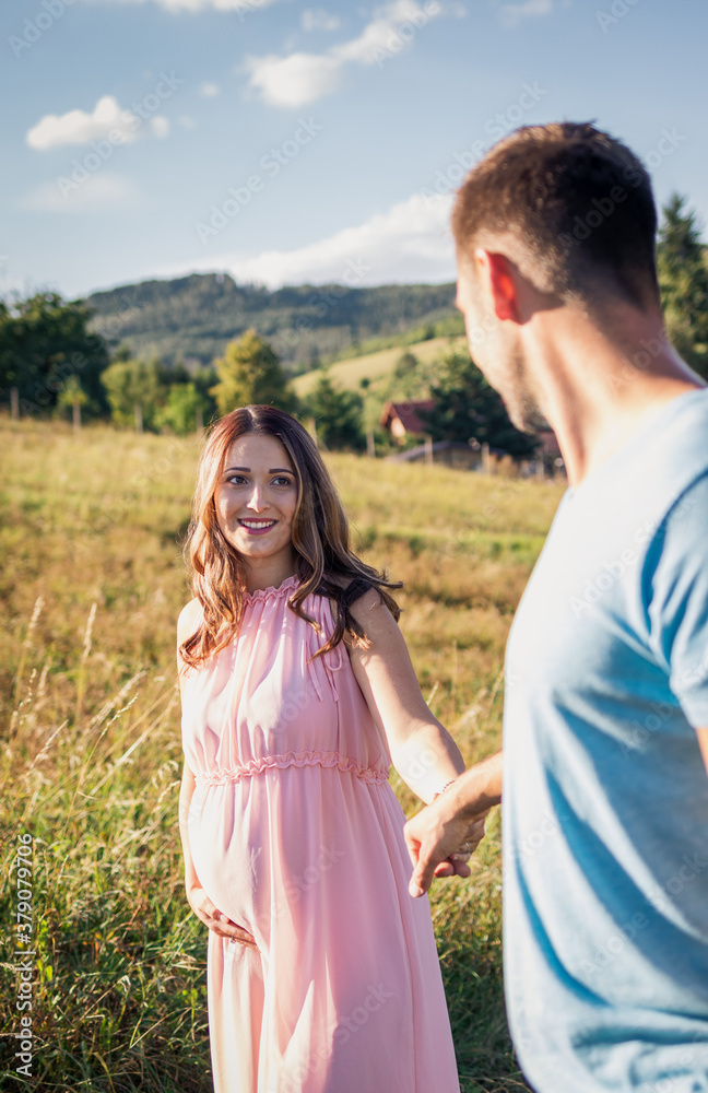 Happy couple expecting baby holding hands. Smiling pregnant woman following her husband Happy couple expecting baby holding hands. Smiling pregnant woman following her husband