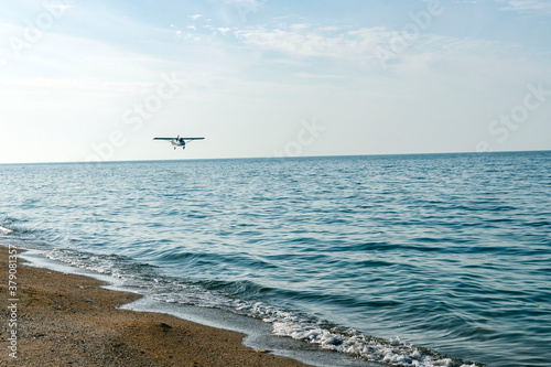 A small plane flies over the sandy seashore.